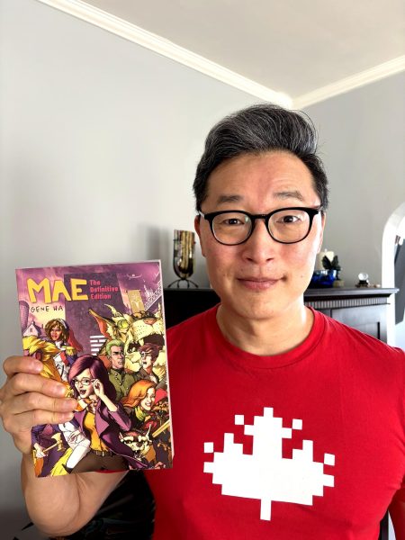 Gene Ha posing with a copy of Mae, a graphic novel that he wrote and illustrated.