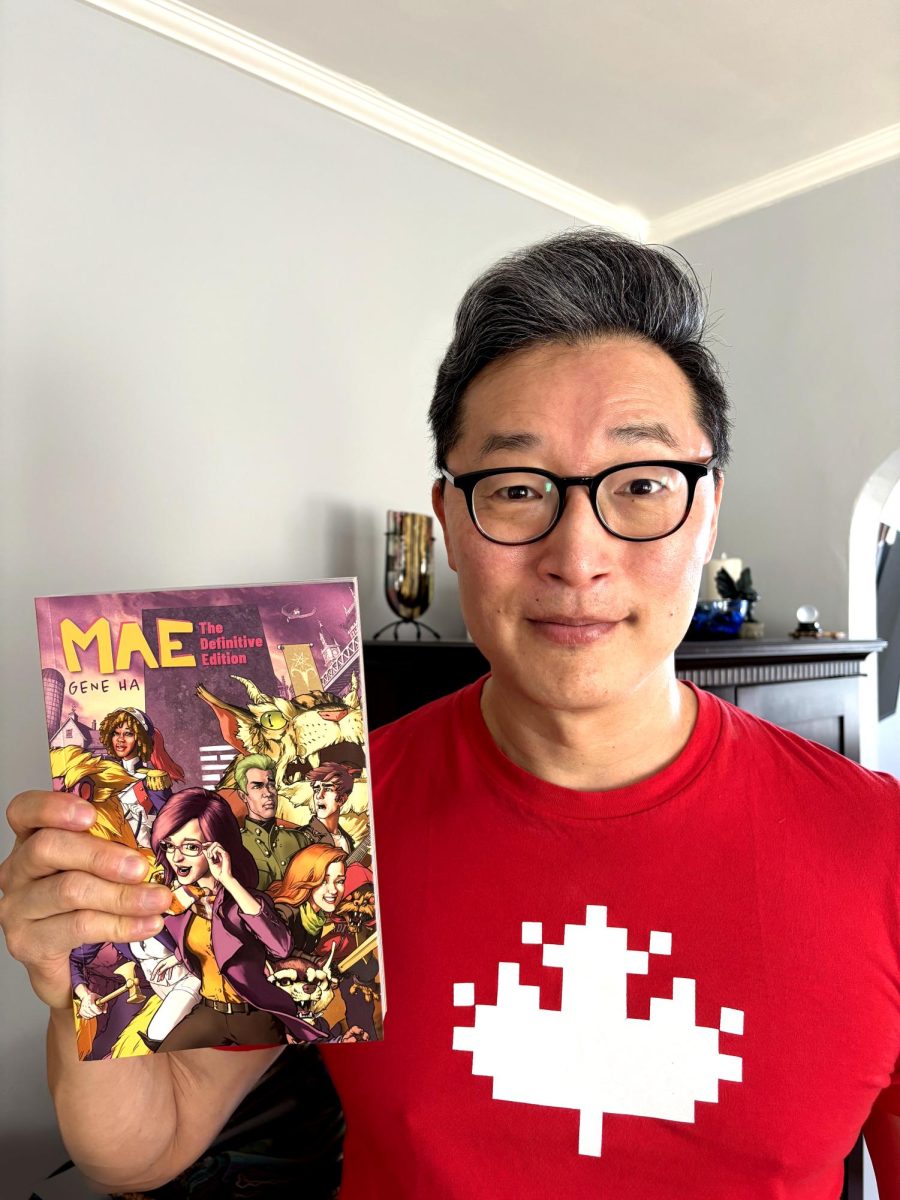Gene Ha posing with a copy of Mae, a graphic novel that he wrote and illustrated.
